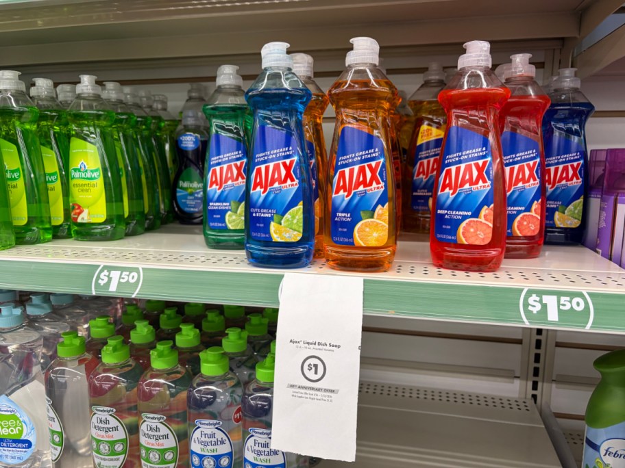 A store shelf displaying multiple bottles of Ajax liquid dish soap with a hanging paper sign advertising a $1 sale price.