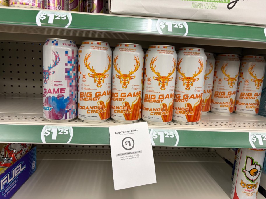A store shelf displaying multiple cans of Big Game Energy drinks with a hanging paper sign advertising a $1 sale price.