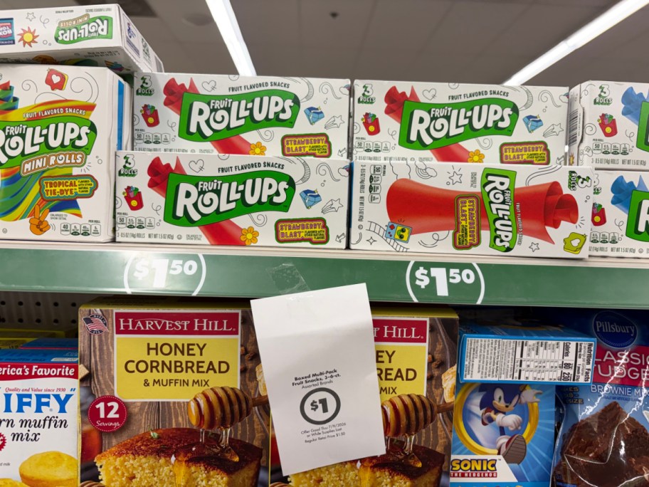 A store shelf displaying boxes of fruit snacks, including Welch's and Fruit by the Foot, with a hanging paper sign advertising a $1 sale price.