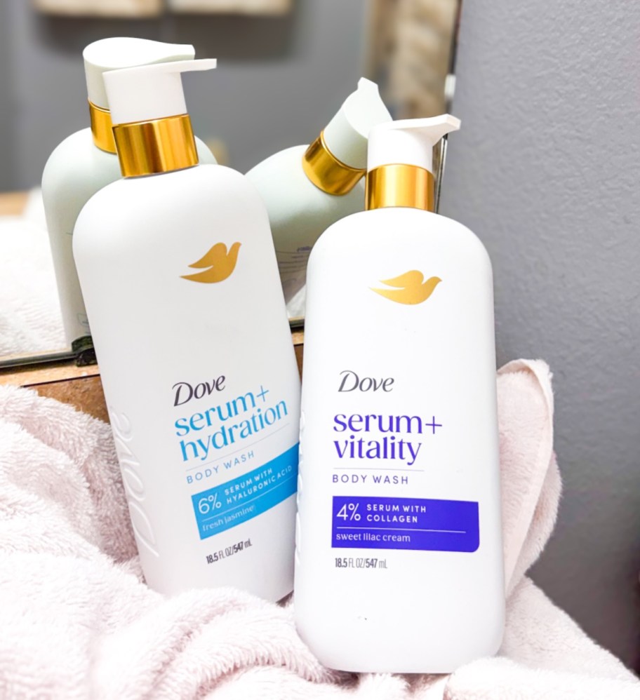 dove serum+ body wash bottles on white bath towel leaning on mirror