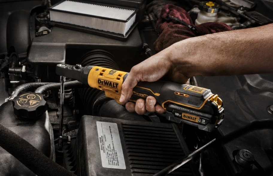 a mans hand using a ratchet on a car engine