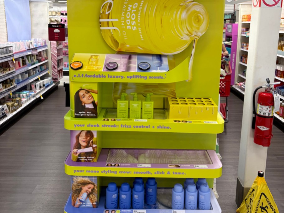 A bright yellow e.l.f. haircare display stand in a retail store aisle, stocked with various hair products.