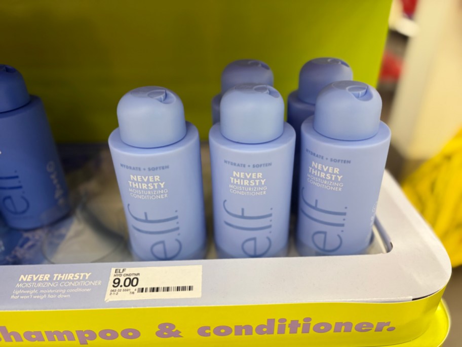 Several light blue bottles of e.l.f. Never Thirsty Moisturizing Conditioner sitting on a yellow store display shelf.