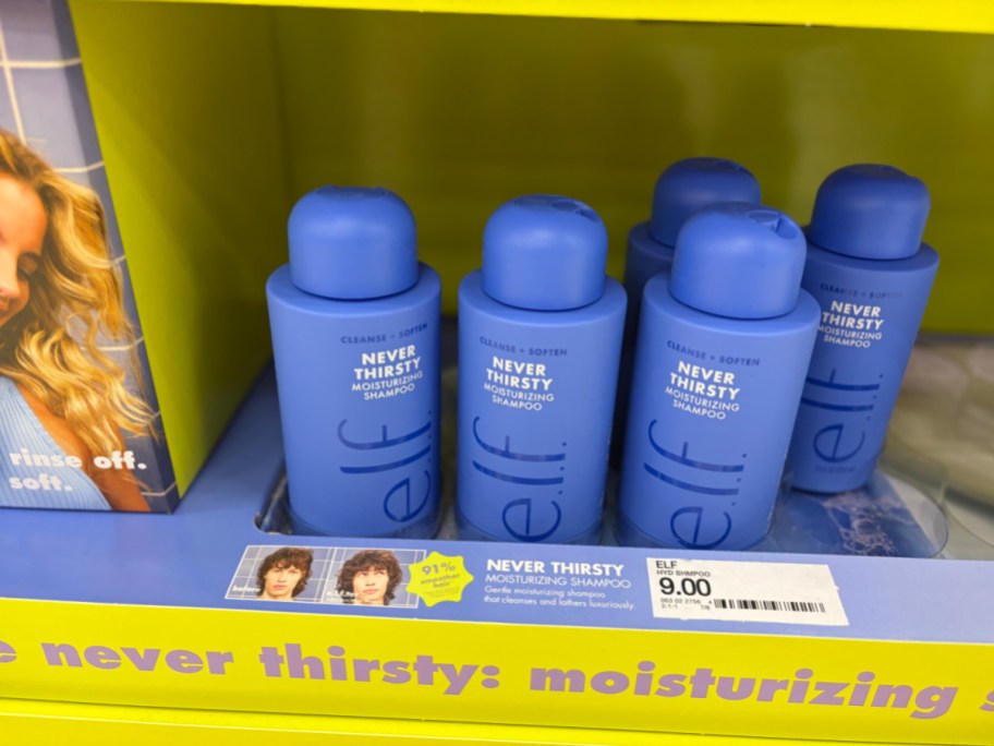 Five blue bottles of e.l.f. Never Thirsty Moisturizing Shampoo sitting on a yellow store display shelf.