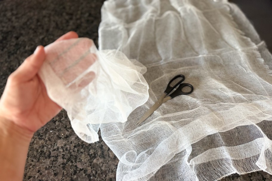 hand holding cheesecloth next to scissors