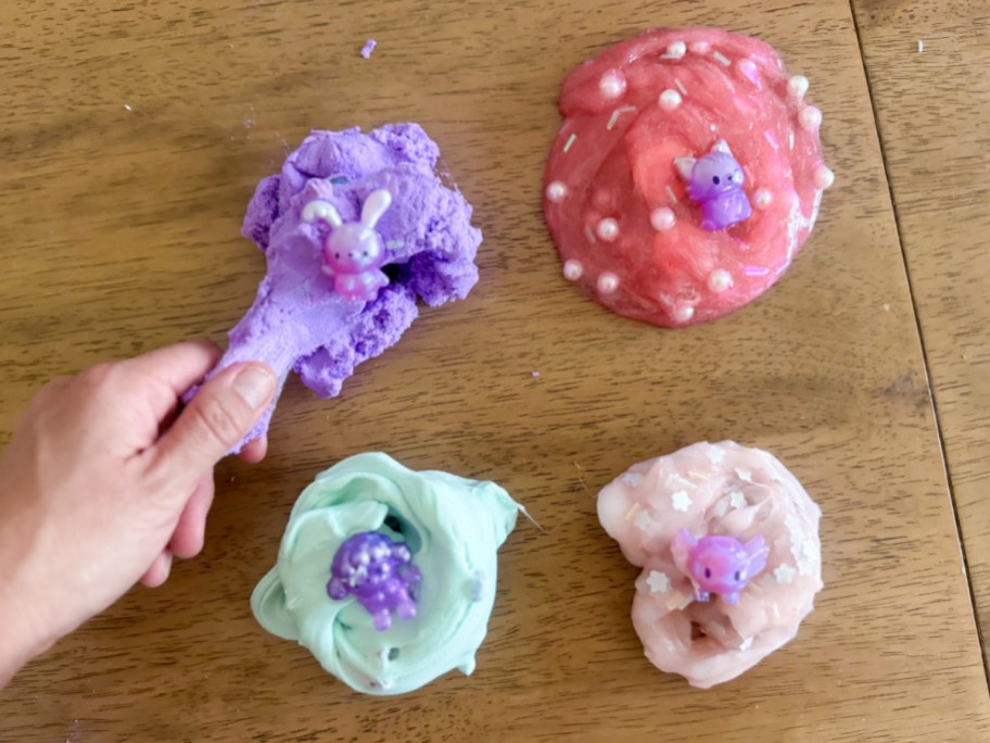 hand grabbing purple slime next to pink, blue, and light pink