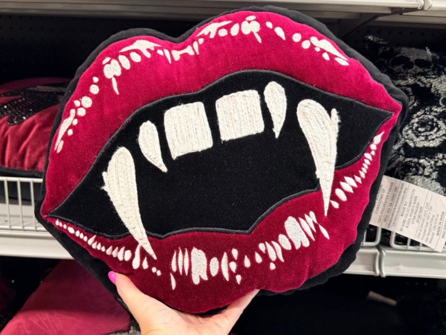 holding a throw pillow shaped like vampire fangs