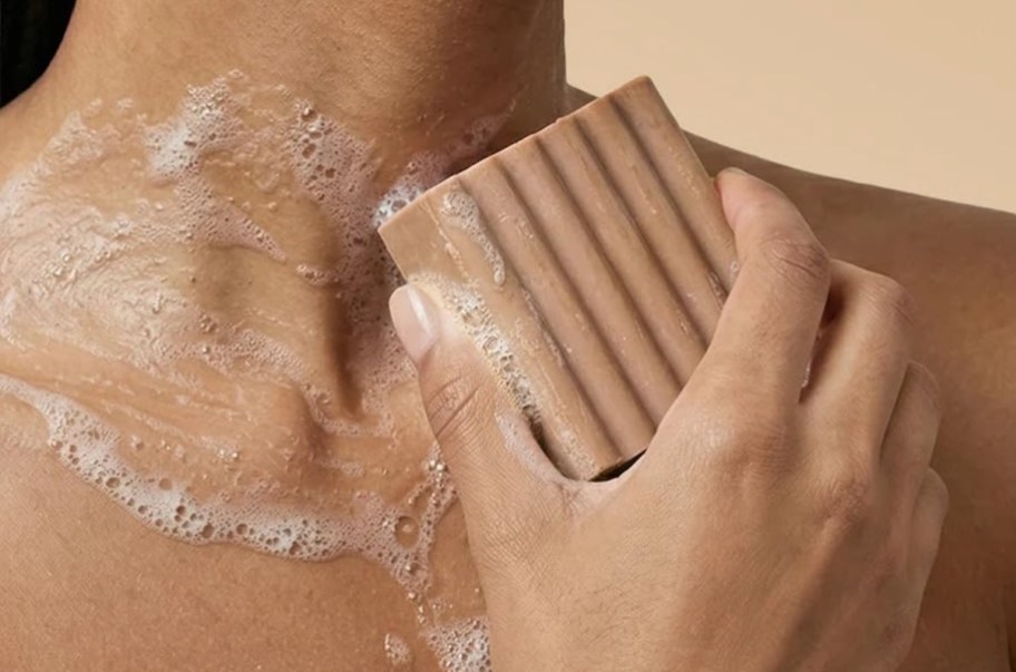 woman washing chest with brown bar of soap