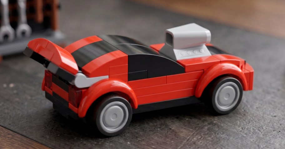 A red and black Lego sports car with a large gray engine scoop sitting on a dark, textured surface.