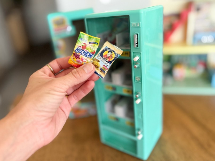 hand holding a mini snack food toy in front of a Mini Brands toy vending machine