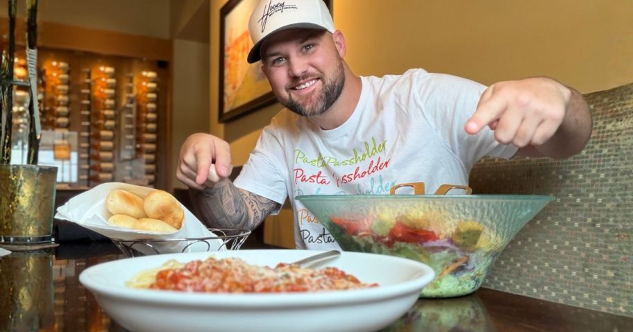 stetson sitting at olive garden pointing at food while wearing pasta pass shirt