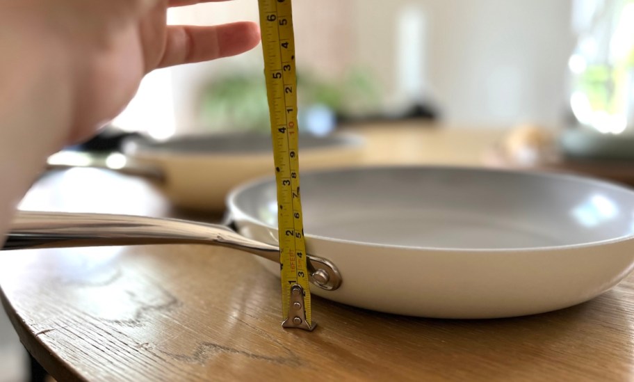 hand holding measuring tape next to saute pan