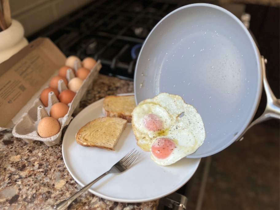 two fried eggs slidding out of pan onto plate with toast