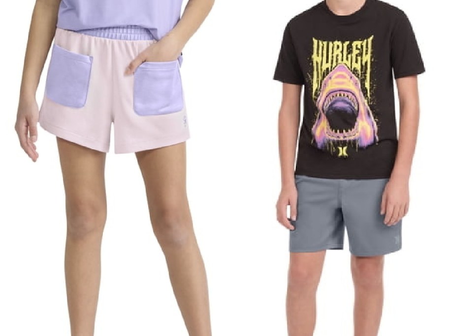 Two children modeling clothing side-by-side: one wearing light pink shorts with large light purple pockets, and the other wearing a black t-shirt with a colorful shark graphic and grey shorts.