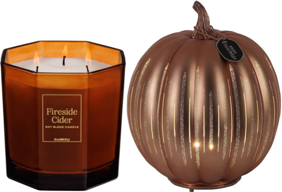 A 24oz Fireside Cider soy blend candle in an amber glass jar next to a metallic bronze decorative pumpkin with light shining through vertical slits.