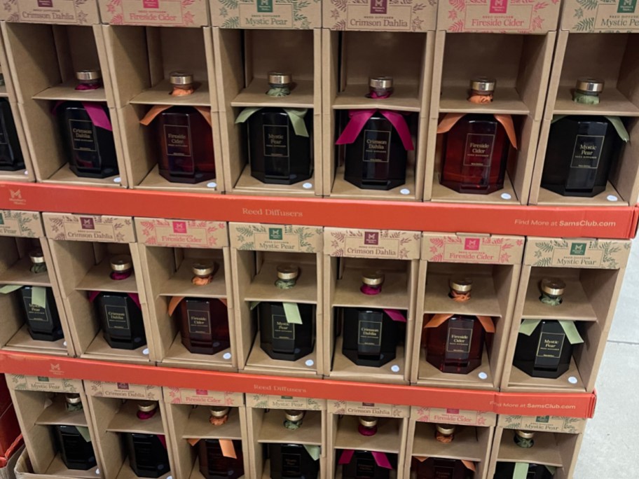 Member's Mark fall reed diffusers in scents like Crimson Dahlia, Fireside Cider, and Mystic Pear displayed in cardboard boxes at Sam's Club.