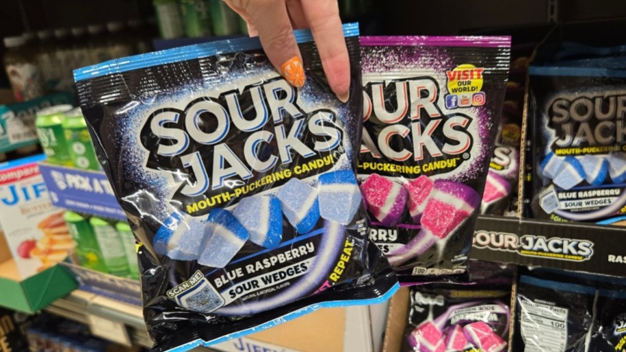 a hand holding two bags of sour candies