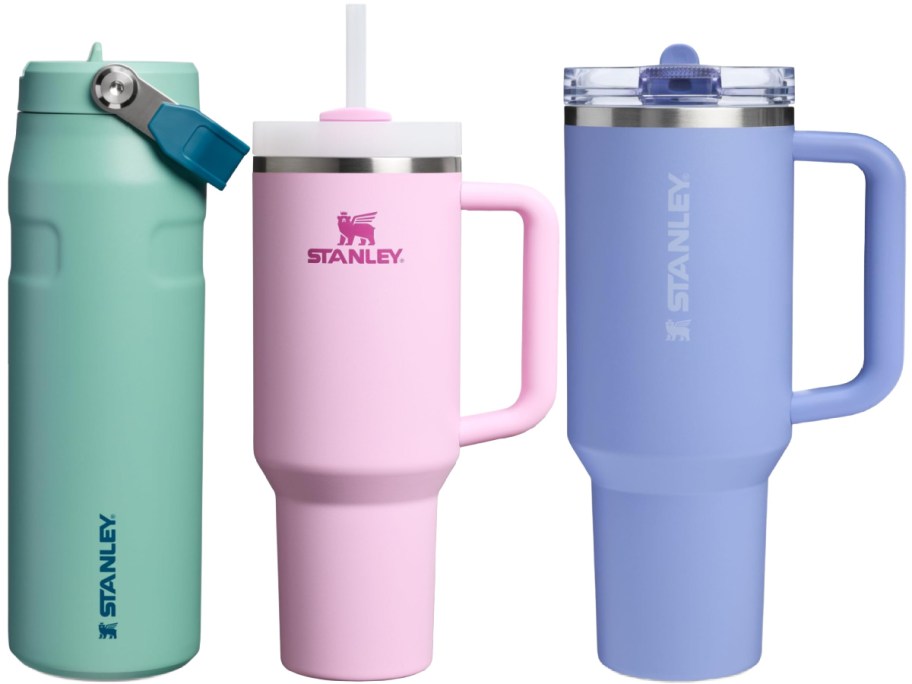 Three Stanley drinkware items: a green water bottle with a handle lid, a pink tumbler with a straw, and a blue tumbler with a handle.