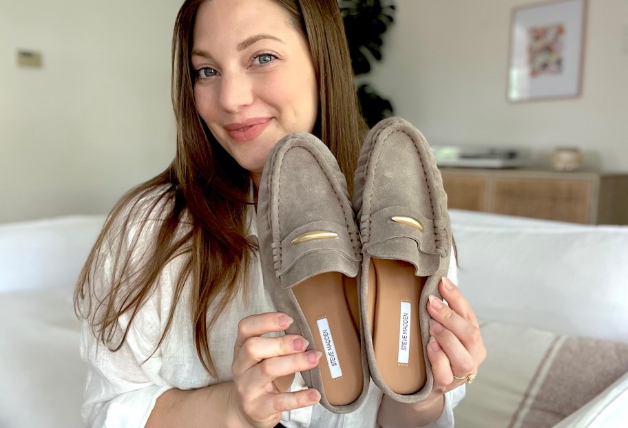 woman holding pair of beige mules