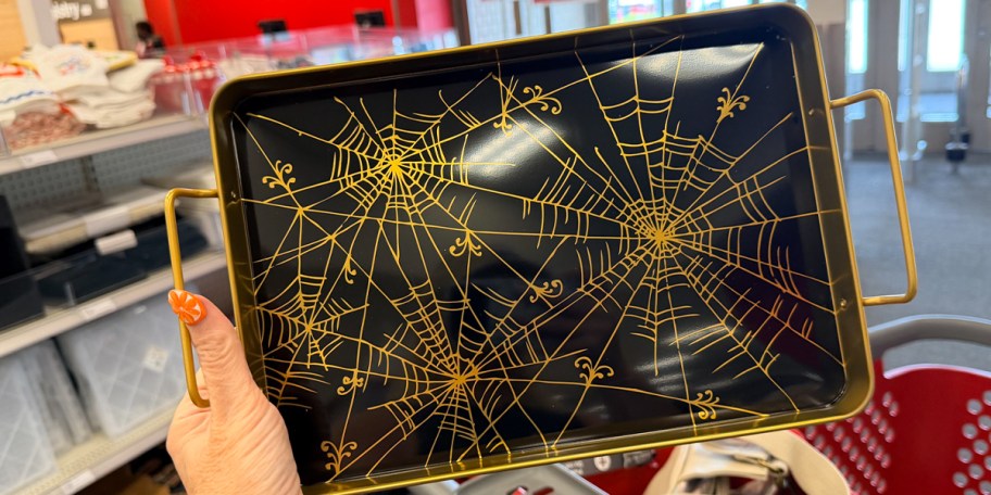 hand holding black and gold serving platter with webs 
