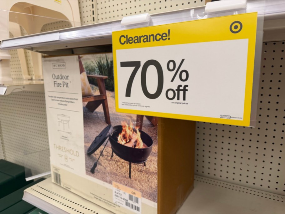 A Target store shelf displaying a boxed Threshold outdoor fire pit with a large yellow sign advertising 70% off clearance.