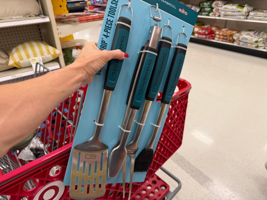 A hand holding a packaged Char-Broil 4-piece grilling tool set over a red Target shopping cart in a store aisle.