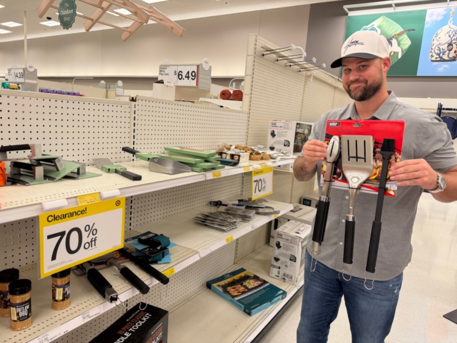 A man holding a packaged 3-piece grilling tool set in a Target store aisle next to shelves displaying large yellow signs advertising 70% off clearance.