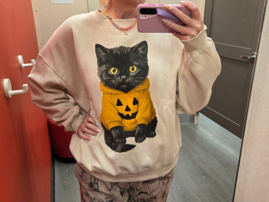 woman wearing a a tan sweatshirt with a black cat in a jack-o-lantern sweatshirt