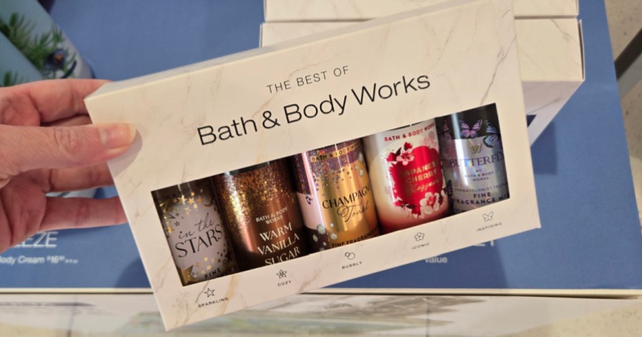 A hand holding a white "The Best of Bath & Body Works" gift box containing five different mini fragrance mists.