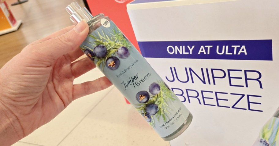A hand holding a bottle of Bath & Body Works Juniper Breeze fragrance mist in front of an Ulta store display.