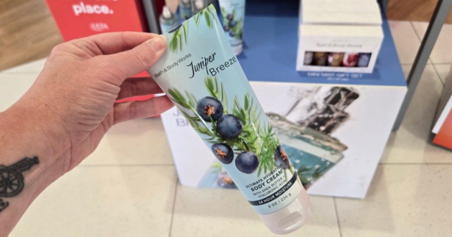 A hand holding a tube of Bath & Body Works Juniper Breeze body cream in a retail store setting.
