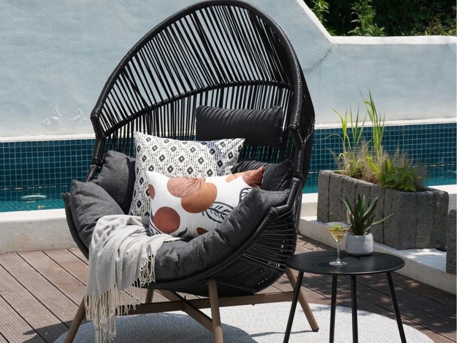 black wicker egg chair outside with fun throw pillows on it 