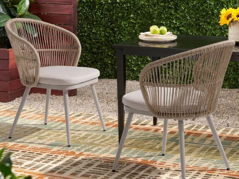 two outdoor wicker chairs on top of a rug and next to an outdoor table