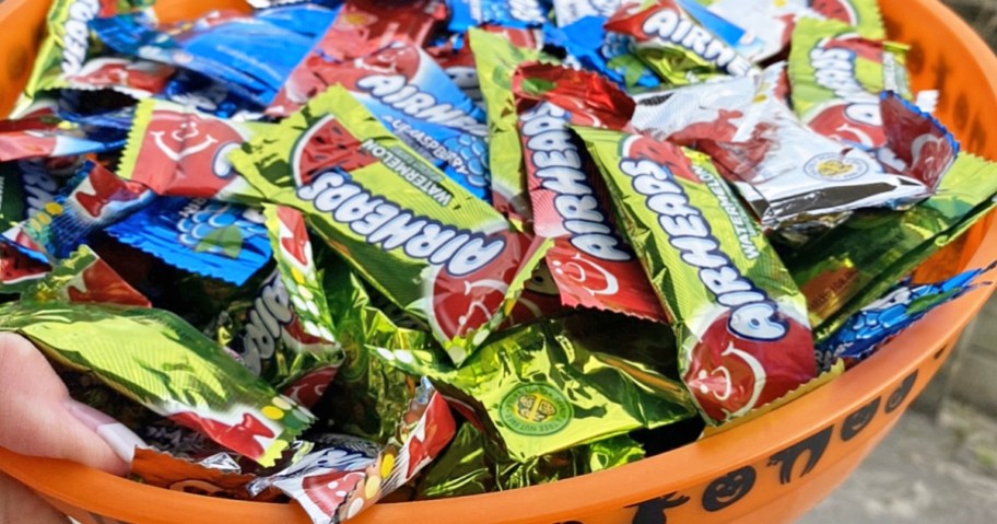 hand holding an orange bowl full of Airheads Mini Candy Bars