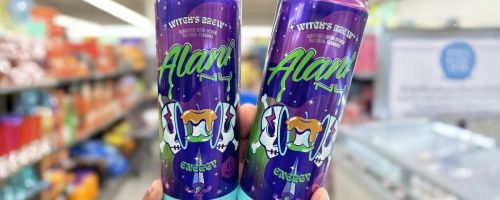 hand holding two Alani Nu Witch's Brew Energy Drink 12oz Cans
