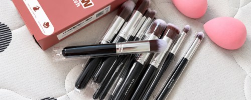 black makeup brushes and two pink makeup sponges with their pink box