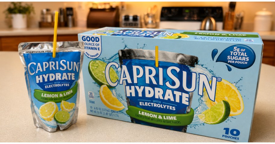 A Capri Sun Hydrate Lemon & Lime juice pouch with a yellow straw standing next to its matching 10-count box on a kitchen counter.