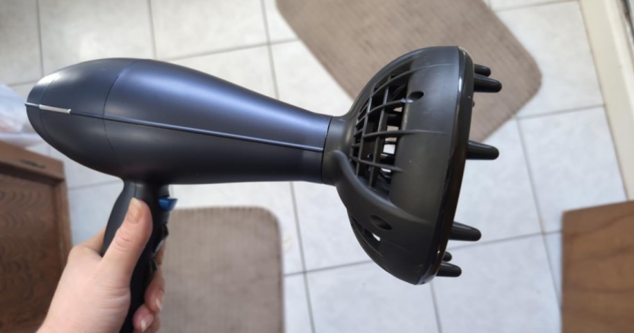 A person holding a dark grey hair dryer with a large diffuser attachment.