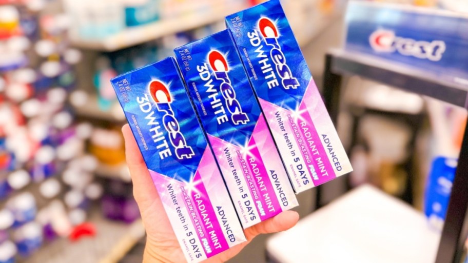 hand holding 3 boxes of crest toothpaste