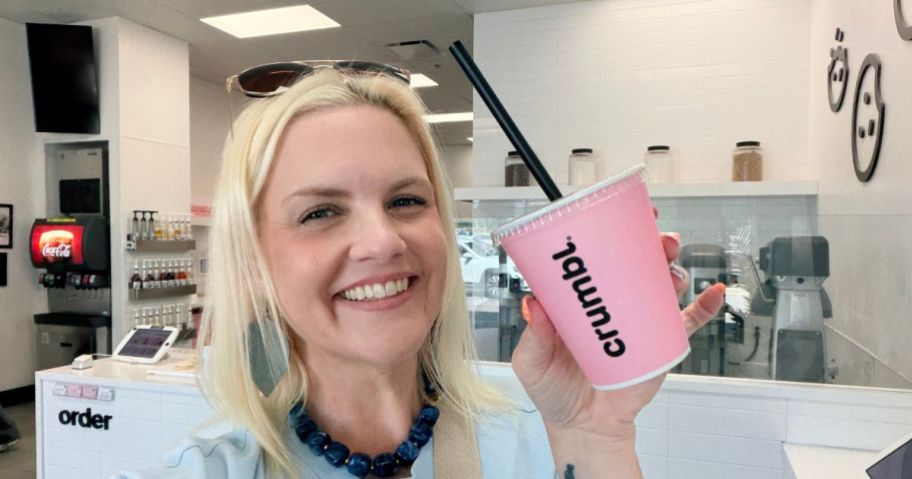 woman holding a pink Crumbl fountain drink cup with a black straw
