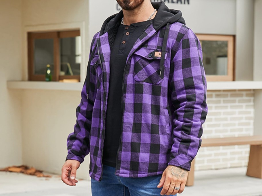 A person wearing a purple and black buffalo plaid flannel hooded jacket over a black shirt and blue jeans.