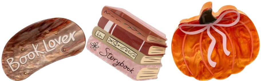 Three decorative hair claw clips featuring a brown tortoiseshell "Book Lover" clip, a stacked books design labeled "Storybook," and an orange marble pumpkin clip with a pink bow.