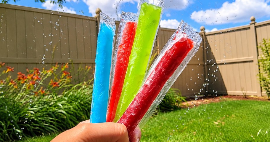 hand holding up colorful freezer pops in a backyard