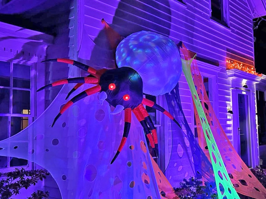 inflatable spider and webs hanging from side of a house in black lights
