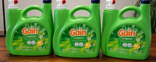 Three bottles of gain laundry detergent on wooden countertop