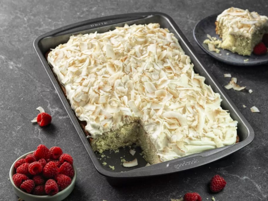 coconut cake inside a baking pan on a counter with bowl of raspberries