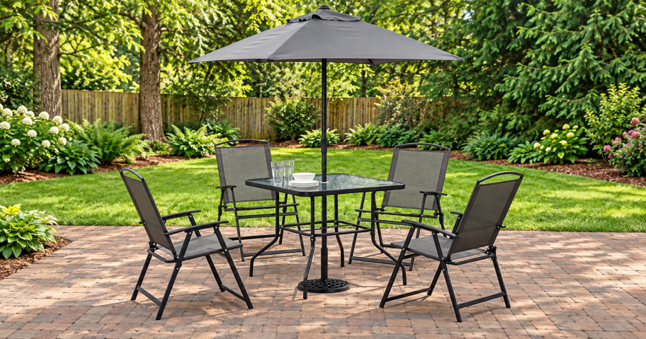 Gray patio dining set with four folding chairs, a square glass table, and matching umbrella on a brick patio.