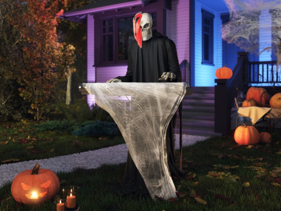 A skeleton keyboard player animatronic wearing a black robe and red hair streak in a front yard decorated with pumpkins and jack-o'-lanterns.