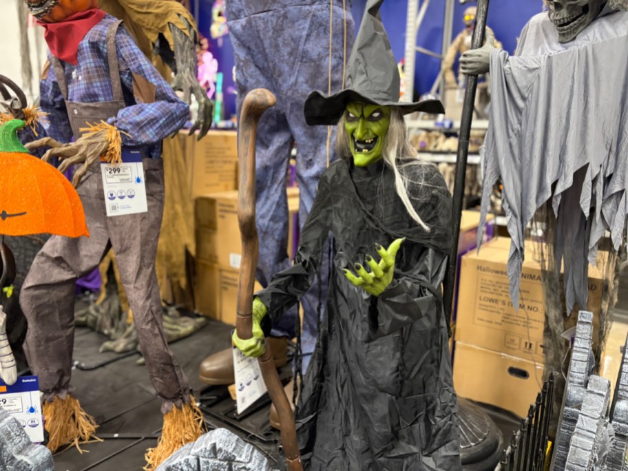 A green-faced witch animatronic wearing a black dress and pointy hat while holding a wooden staff in a store display.