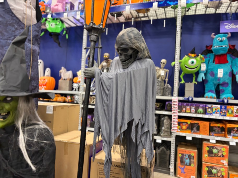 A hooded skeleton ghoul animatronic wearing tattered grey robes and holding an orange gaslight lamp in a store display.